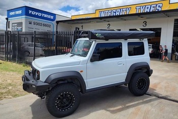  White Suzuki Jimny with roof rack and off-road wheels at tyre workshop
